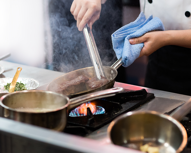 Imagebild Restaurant: Koch steht am Herd und brät Steaks an